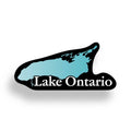 A die-cut sticker or decal shaped like the outline of Lake Ontario, with a black border, a light blue lake fill, and the words "Lake Ontario" in white across the center, shown on a white background with a soft drop shadow. Anti Trump Sticker